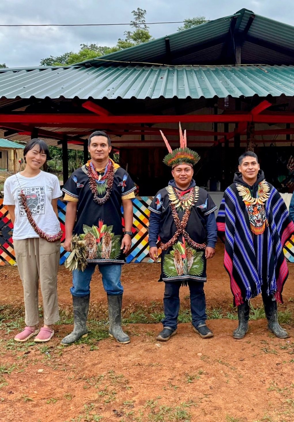 Min standing with the taitas in traditional dress in front of the ceremonial maloca