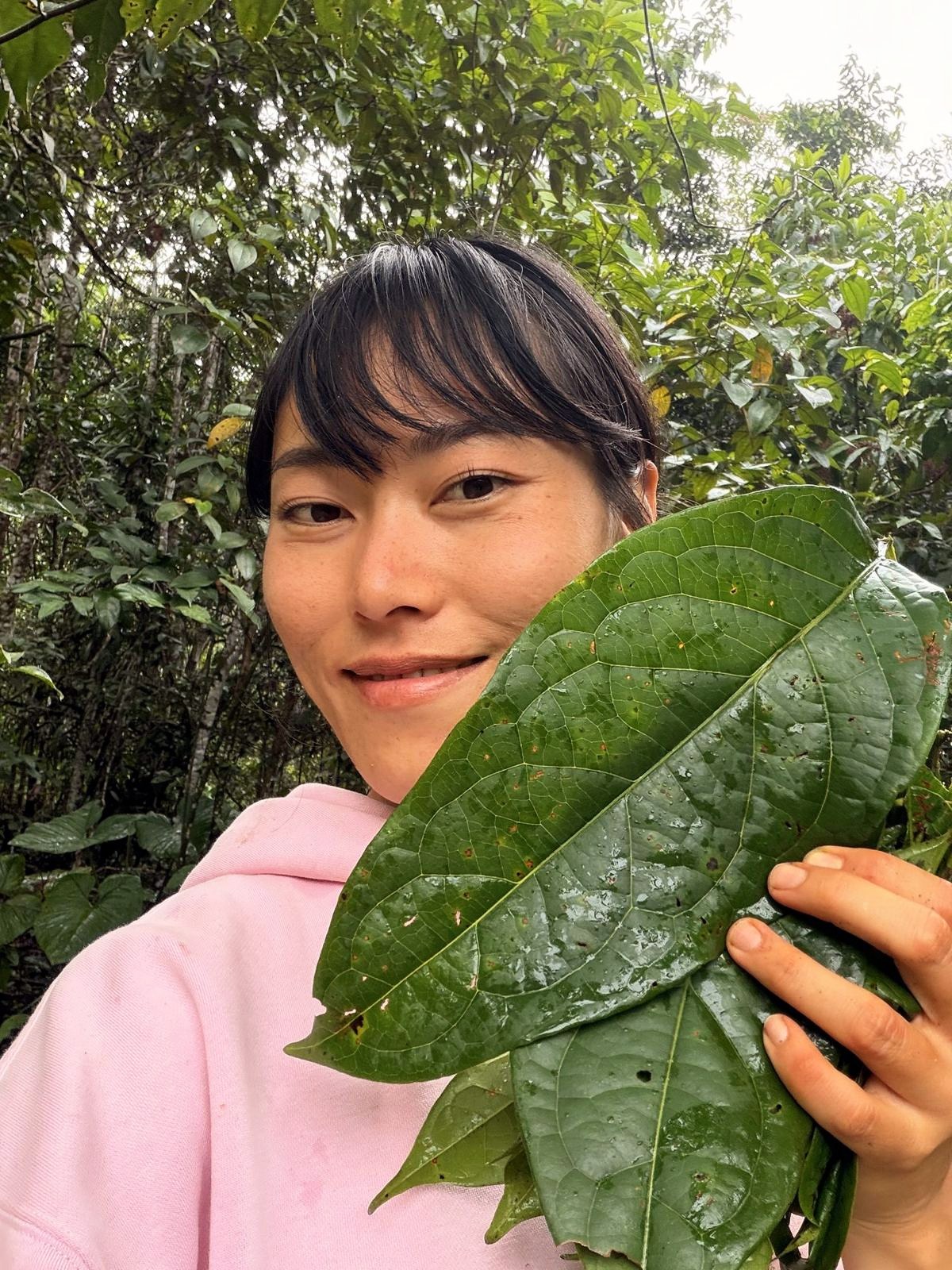 Min holding a large leaf in the forest